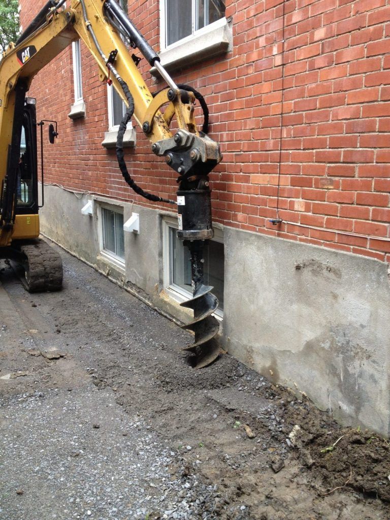 Tarière hydraulique forant des trous le long du mur de brique d'un bâtiment