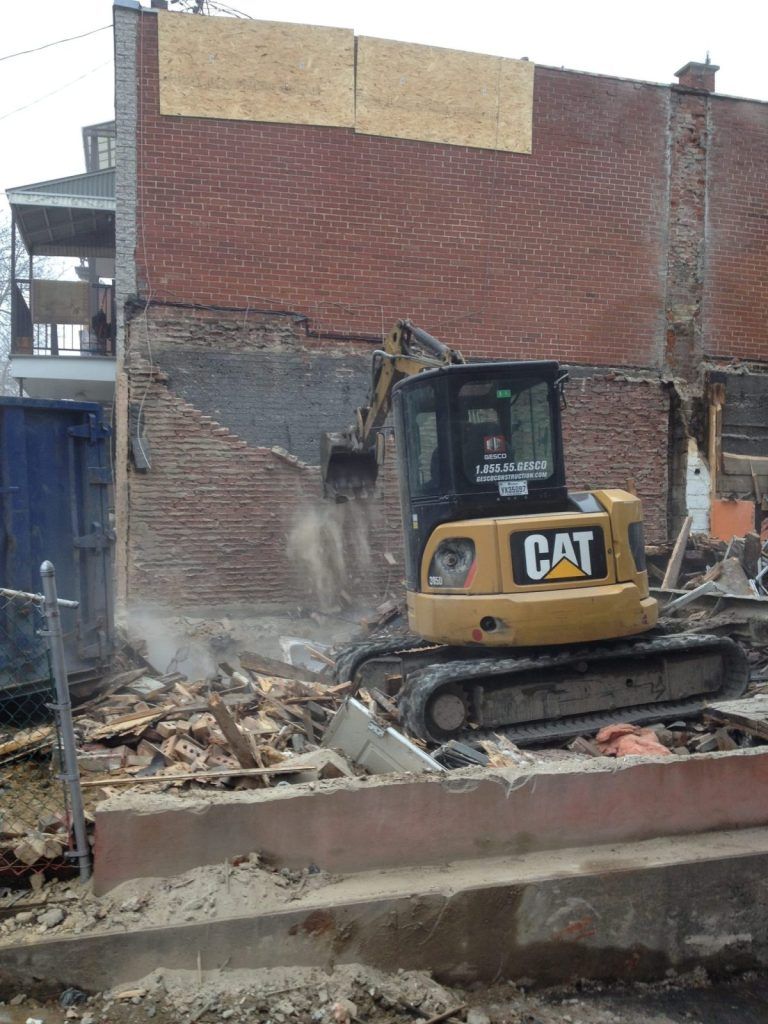 Pelle mécanique CAT démolissant le mur de brique d'un bâtiment en milieu urbain