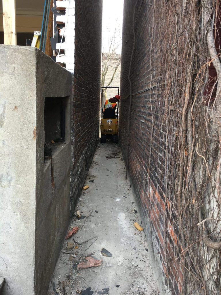 Corridor étroit entre deux bâtiments avec une mini-excavatrice au fond du passage