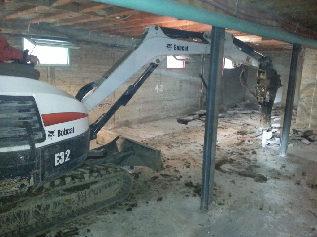 Chargeur compact Bobcat E32 cassant une dalle de béton à l'intérieur d'un sous-sol