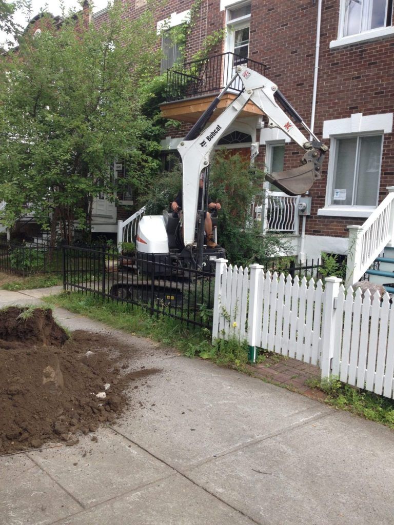 Terrain excavé en cour avant d'une résidence, clôture de bois blanche préservée
