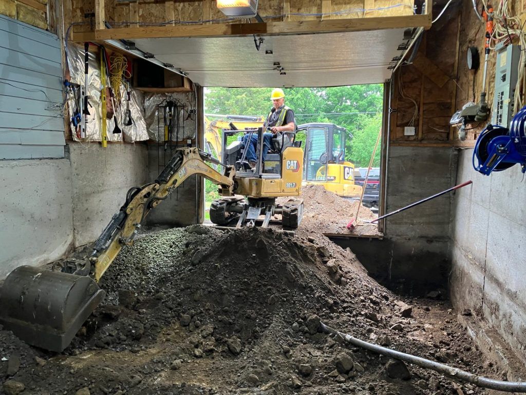 Mini-excavatrice creusant sous un abri de voiture en espace restreint