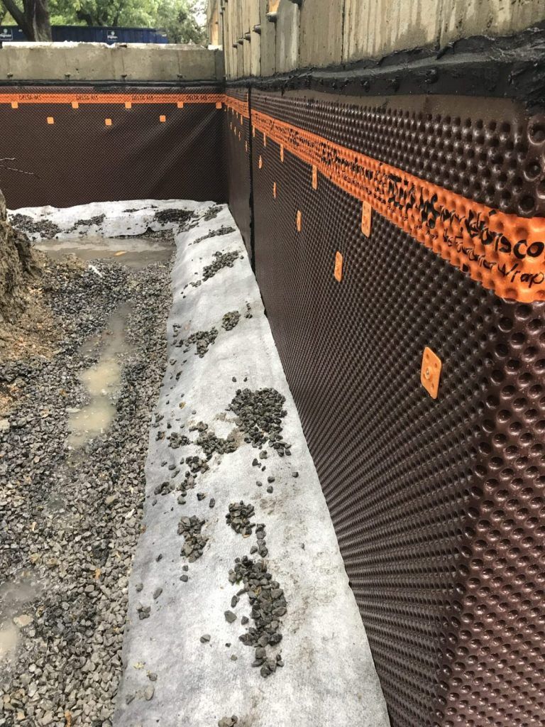 Membrane drainante alvéolée posée sur un mur de fondation avec lit de pierre concassée
