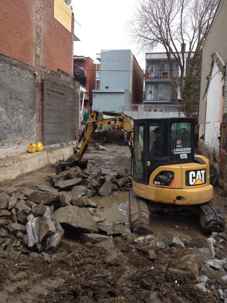Mini-excavatrice CAT brisant le roc au fond d'un creusage de sous-sol